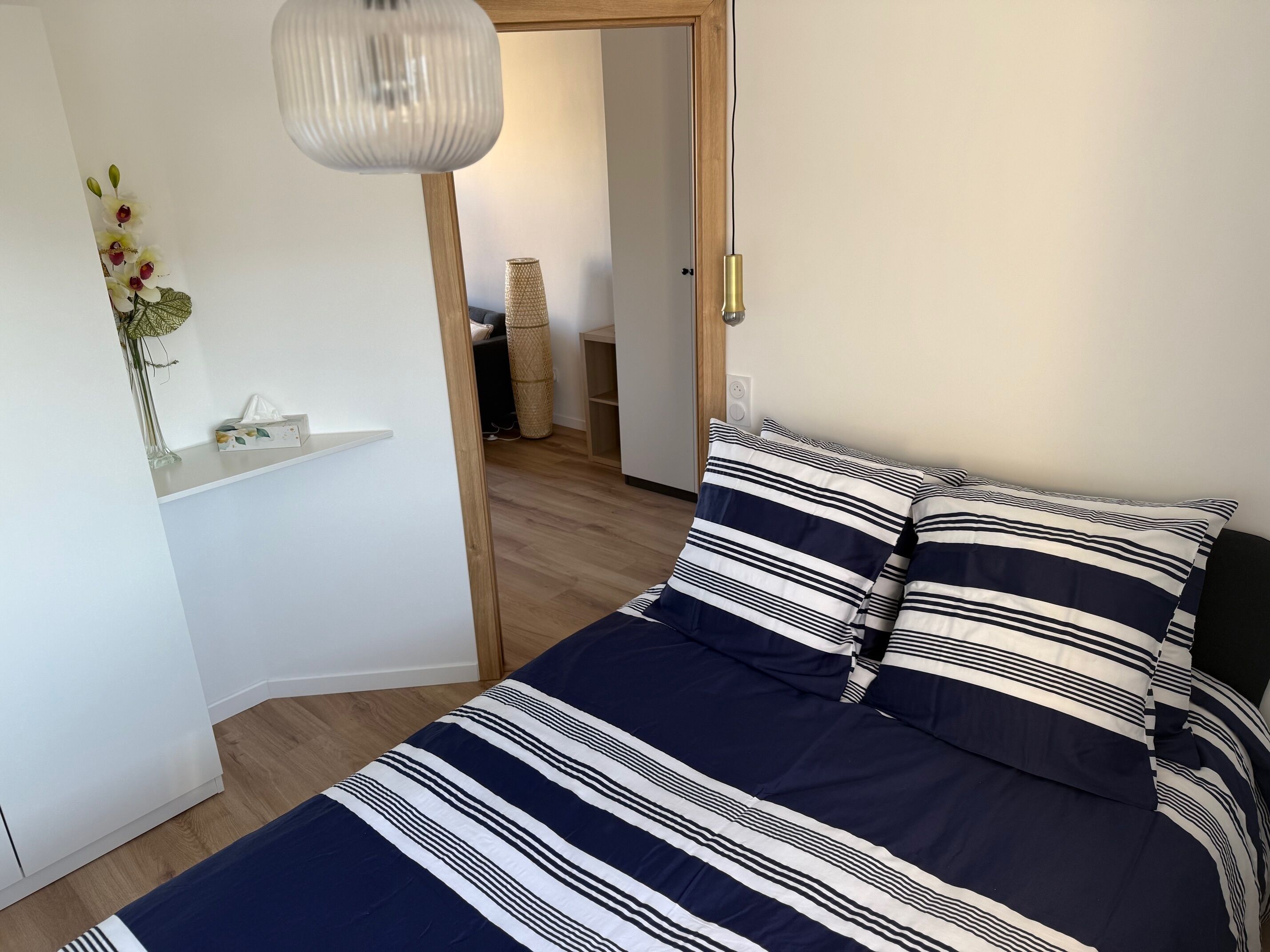 A bedroom with a bed, a bedside table, a lamp, and a door leading to another room.