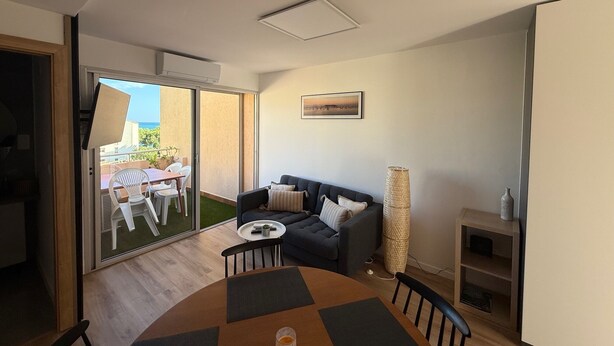 A modern living room with a round table, a sofa, and a balcony with outdoor furniture.