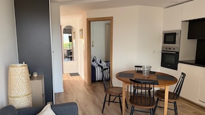 A modern living room with a sofa, a dining table with chairs, and a kitchen area with appliances.
