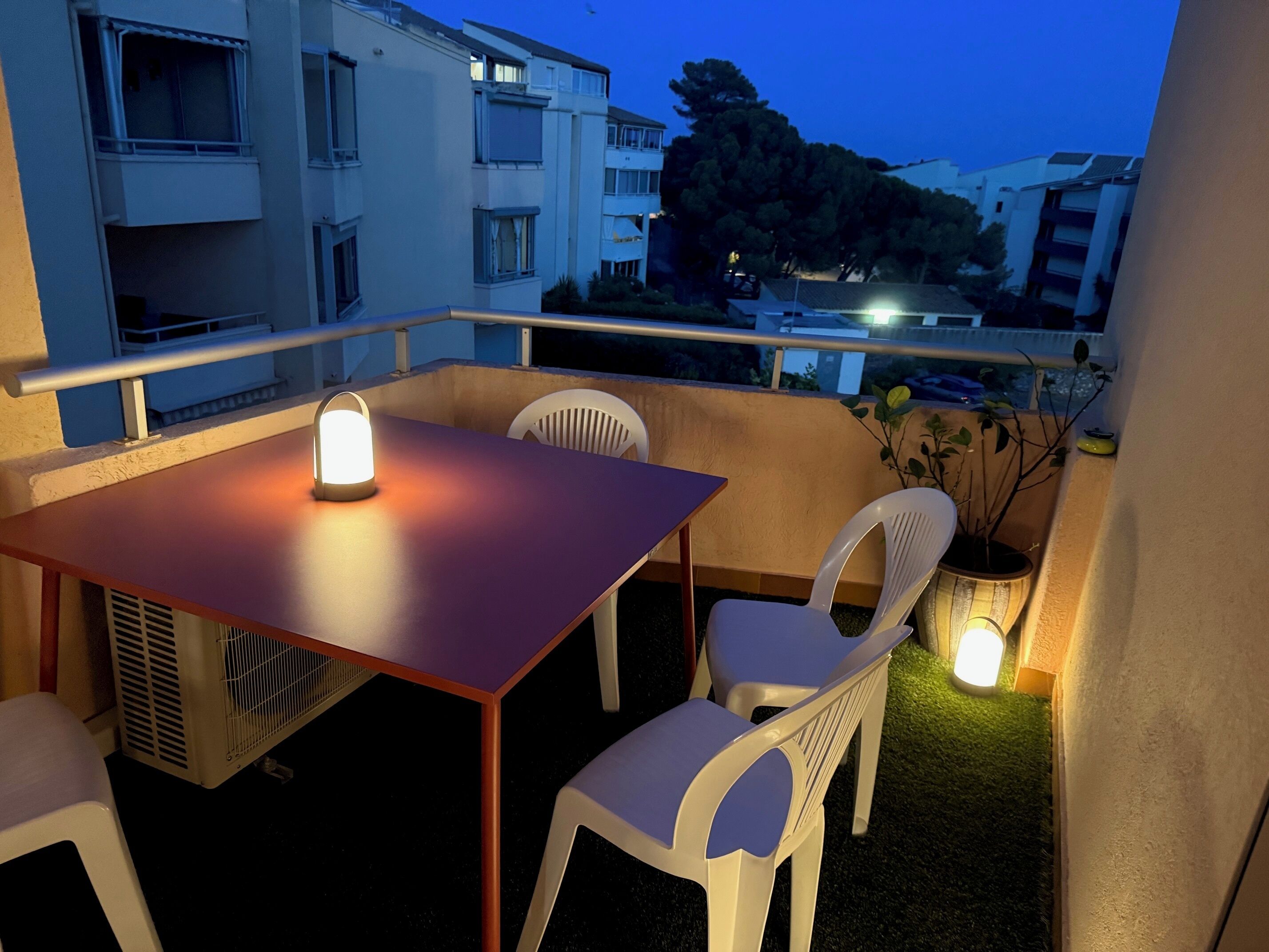 A balcony with a table and chairs, a lantern, and a potted plant.