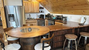 Una cocina con una isla de madera, taburetes de bar y un refrigerador de acero inoxidable.