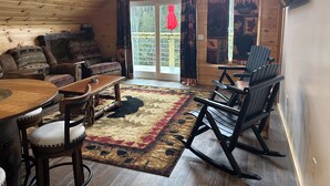 Interior acogedor de una cabaña con techo de madera, una mesa de comedor, un sofá y una mecedora.