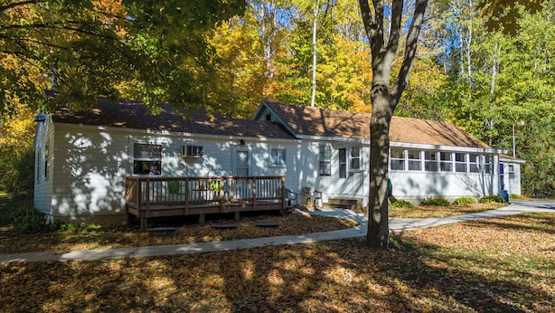 A two-story house with a porch, surrounded by trees with autumn foliage.