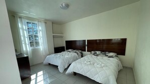 A hotel room with two beds, a desk, a window with curtains, and a ceiling light. - Hotel Leilani (Asunción Nochixtlán)