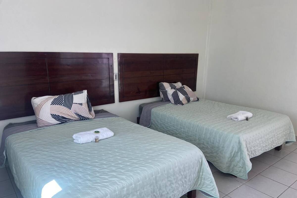 Two twin beds with matching headboards and green bedspreads, each with a pillow and a rolled towel.