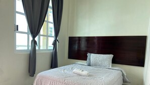 A neatly made bed with a white comforter and a folded towel, a wooden headboard, and a window with curtains. - Hotel Leilani (Asunción Nochixtlán)