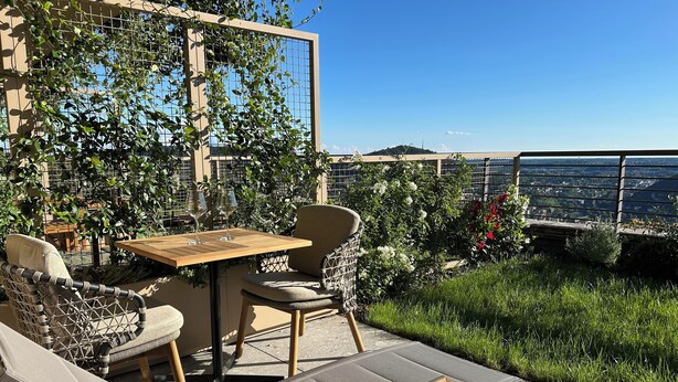 An outdoor patio with a table and chairs, surrounded by greenery and a view of the cityscape. - Exclusive flat on Lake Como with panoramic views (Como)