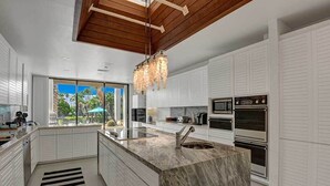 Una cocina moderna con armarios blancos, una isla de mármol y vistas a palmeras.