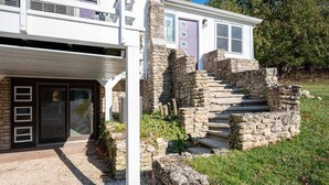 Une maison moderne à deux étages, dotée d’un escalier en pierre menant à la porte d’entrée, et entourée d’une pelouse bien entretenue.