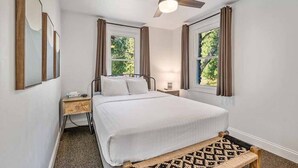 Une chambre à coucher avec un lit, une table de chevet, un ventilateur de plafond et des fenêtres avec des rideaux.