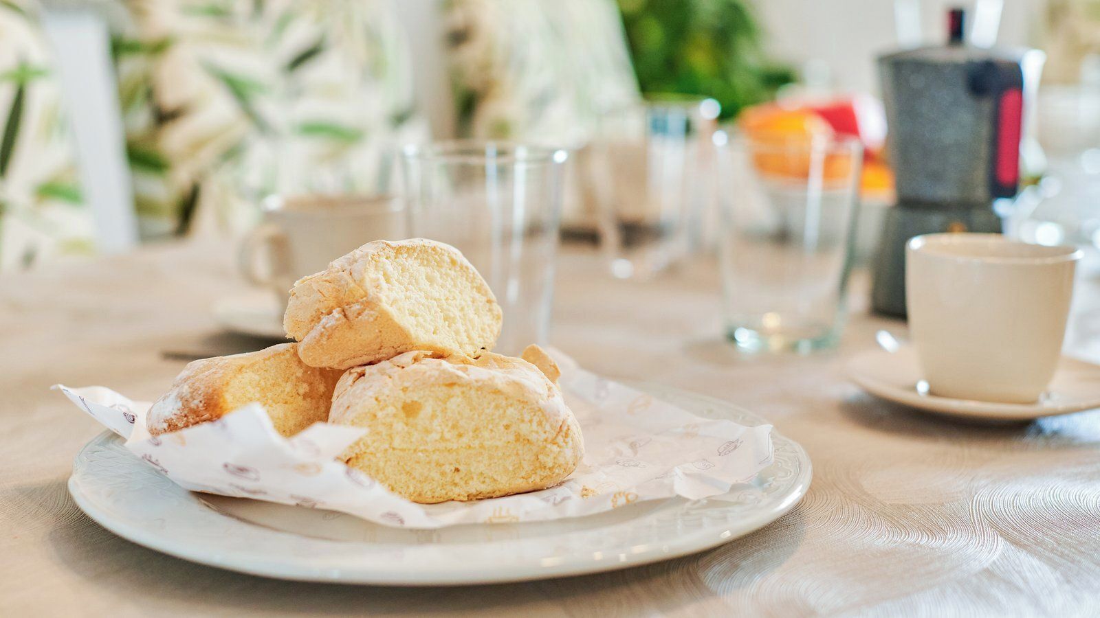 A plate with three biscuits on a table with a cup and saucer in the background.