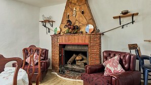 Ein gemütliches Wohnzimmer mit Kamin aus Backstein, Ledersofas und Holzstühlen.