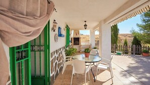 Eine Terrasse mit einem runden Glastisch und weißen Stühlen, einer grünen Tür und einer Steinmauer.