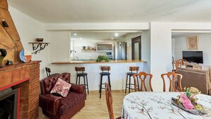 Ein gemütliches Wohnzimmer mit Kamin, ein Essbereich mit Tisch für vier Personen und eine Küche im Hintergrund.