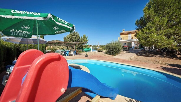Ein Swimmingpool mit Rutsche, umgeben von Bäumen und einem Gebäude.