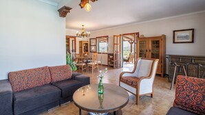Een ruime woonkamer met een bank, fauteuil en salontafel. Achterin is een eethoek met stoelen en een tafel.