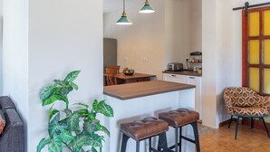 Een compacte leefruimte met een keukenhoek, een eettafel en een barkruk.