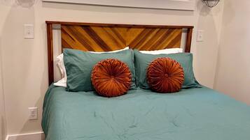 Un dormitorio con cabecera de madera, ropa de cama color verde azulado y dos almohadas decorativas anaranjadas.