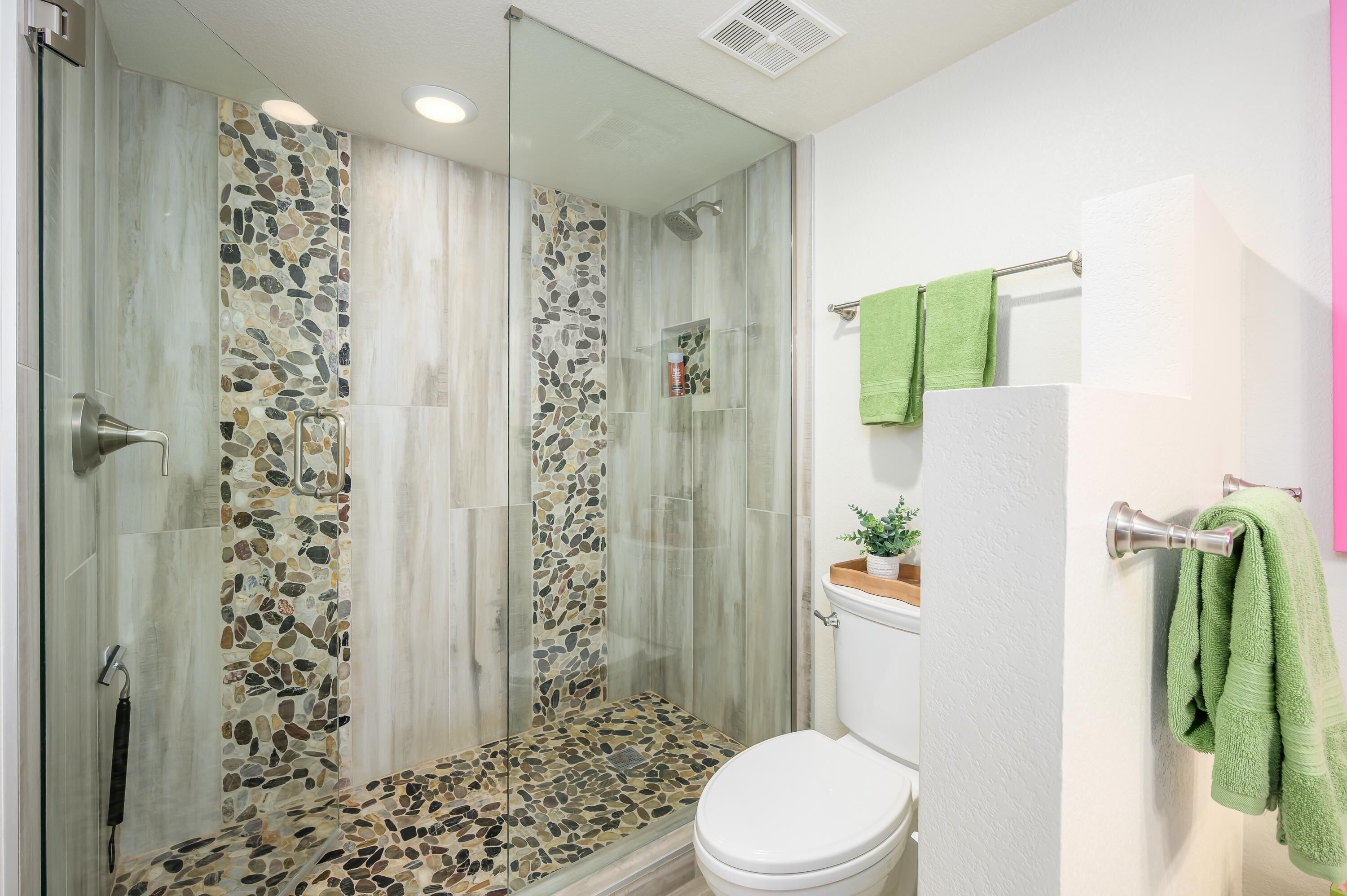 Une salle de bain avec une douche à parois de verre, des toilettes et un porte-serviettes avec des serviettes vertes.
