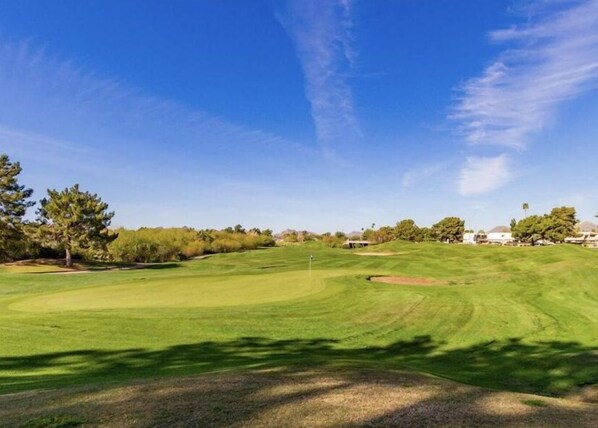 Un campo de golf con cielo despejado, césped cuidado y árboles.