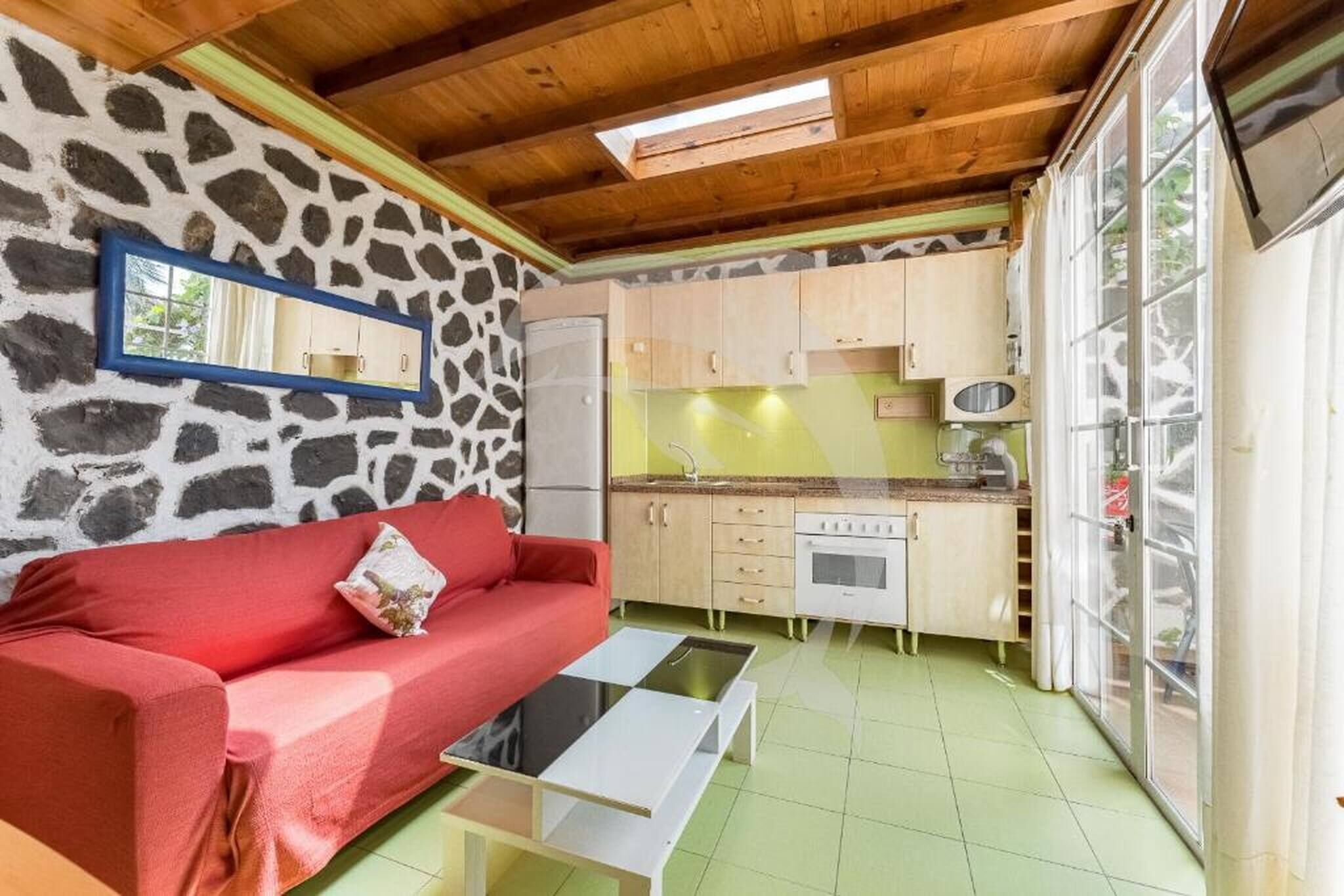 A compact kitchen with a stone wall, a red sofa, and a small dining table.