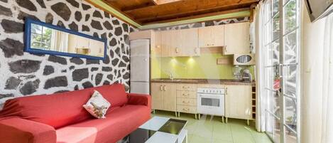 A compact kitchen with a stone wall, a red sofa, and a small dining table.