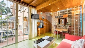 A cozy interior with a wooden ceiling, a glass door leading outside, a dining area with a table and chairs, and a red sofa. - Relax in El Médano's Hidden Gem 1-bedroom Apartment (Granadilla de Abona)