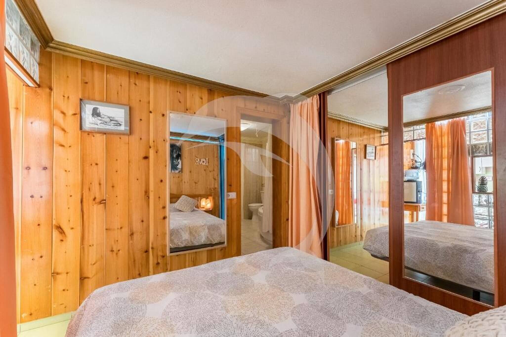 Una habitación con paneles de madera, una cama, un espejo y una puerta que da al baño.