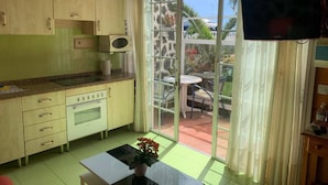 A compact kitchen with a microwave, stove, and cabinets, leading to a patio with a table and chairs. - Relax in El Médano's Hidden Gem 1-bedroom Apartment (Granadilla de Abona)