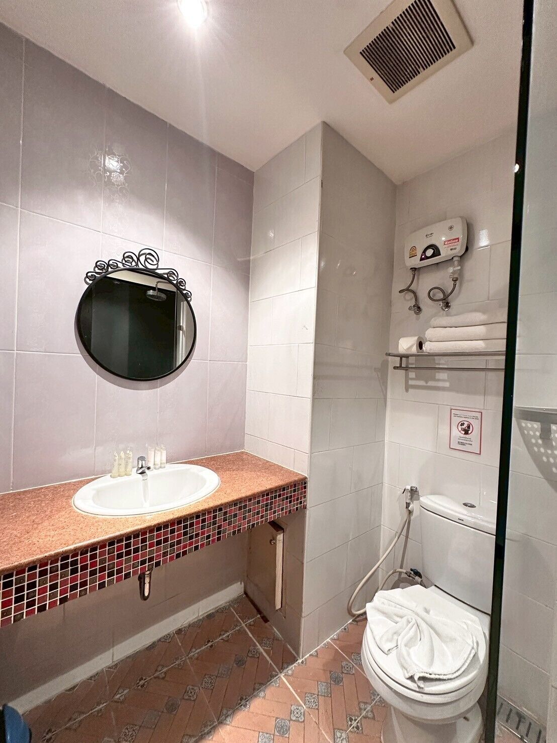 A bathroom with a round mirror, a sink, a toilet, and a shower area.