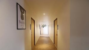 Un pasillo con piso de madera, obras de arte enmarcadas en la pared izquierda y puertas a ambos lados que dan a habitaciones.