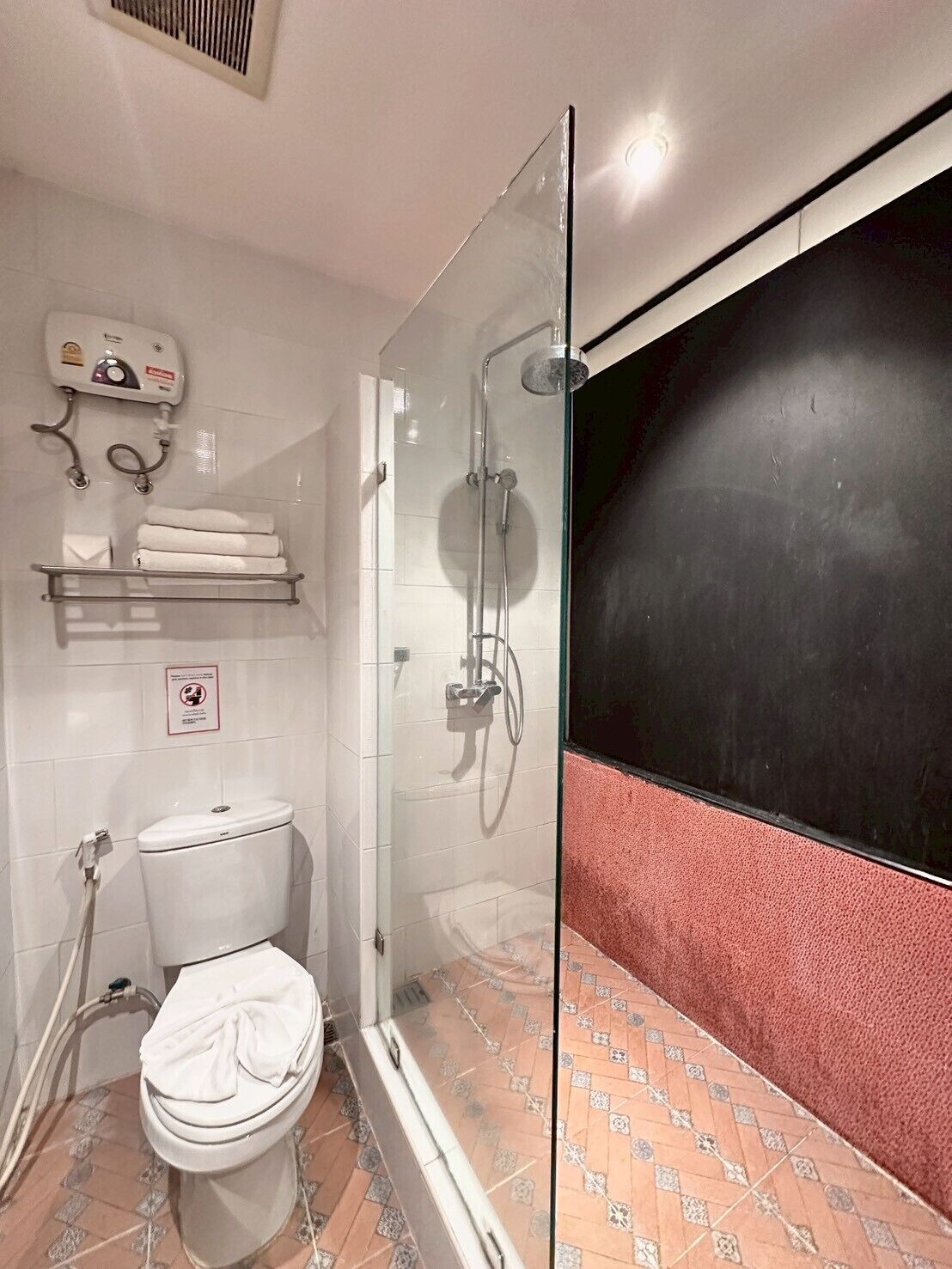 A bathroom with a glass-enclosed shower, a toilet, a towel rack, and a hand dryer.