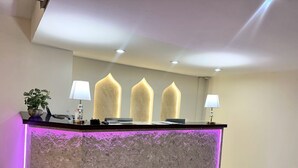 Un mostrador de recepción con fachada de piedra texturizada, tres columnas altas iluminadas y dos lámparas fijadas a la pared.