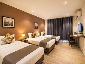 A hotel room with two beds, a desk, a TV, and a cityscape painting on the wall. - STUDIO F SUKHUMVIT (Bangkok)