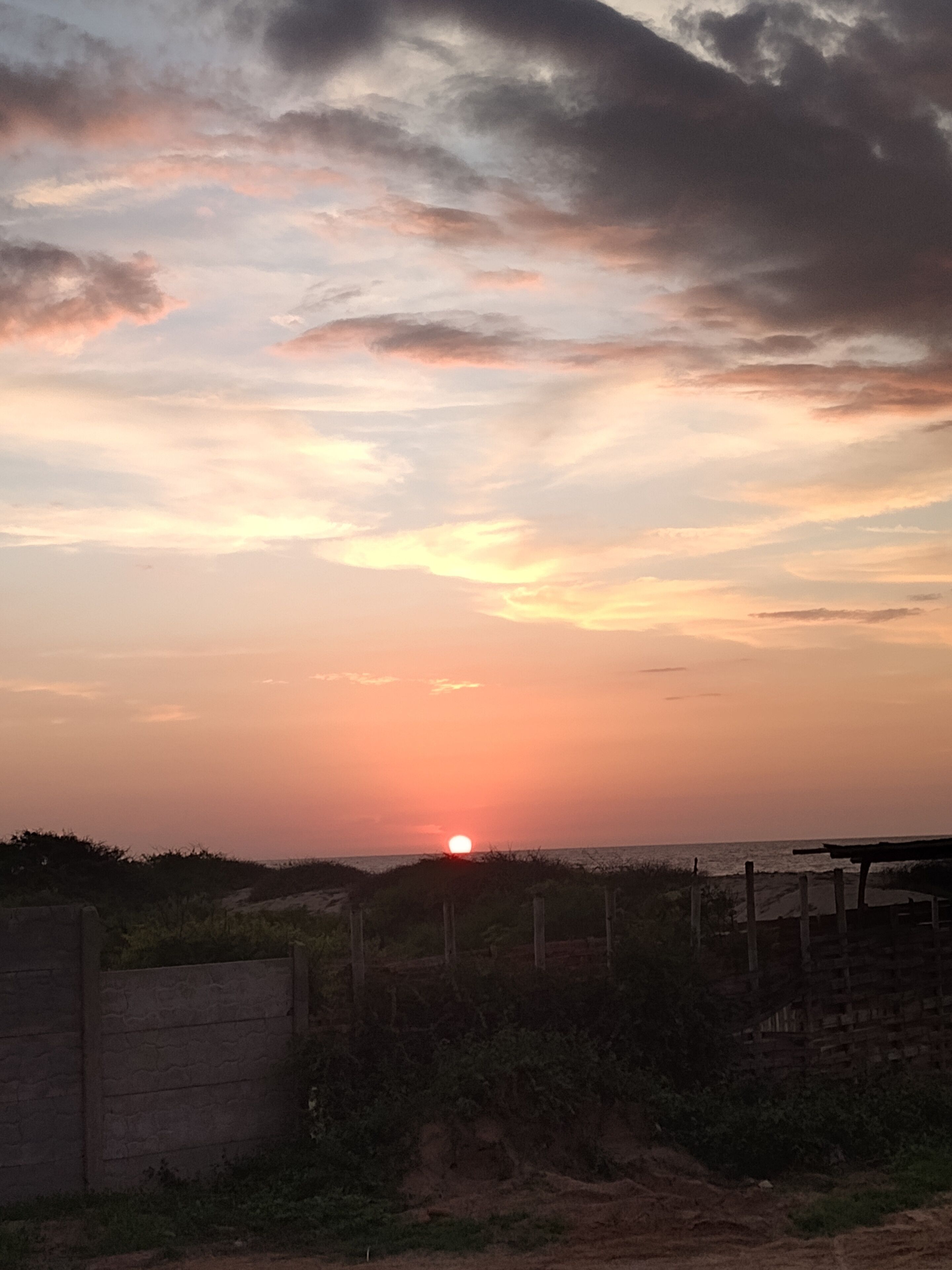A sunset over a beach with a fence and a wall in the foreground.