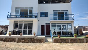 A two-story building with balconies, large windows, and a stone wall in front. - Delightful 4bedroom house in Plateritos,Canoas d Punta Sal,Contralmirante Villar (Tumbes)
