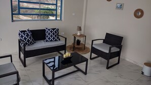A modern living room with a sofa, two chairs, a coffee table, and a small side table. A large window offers a view of a bridge and hills. - Delightful 4bedroom house in Plateritos,Canoas d Punta Sal,Contralmirante Villar (Tumbes)