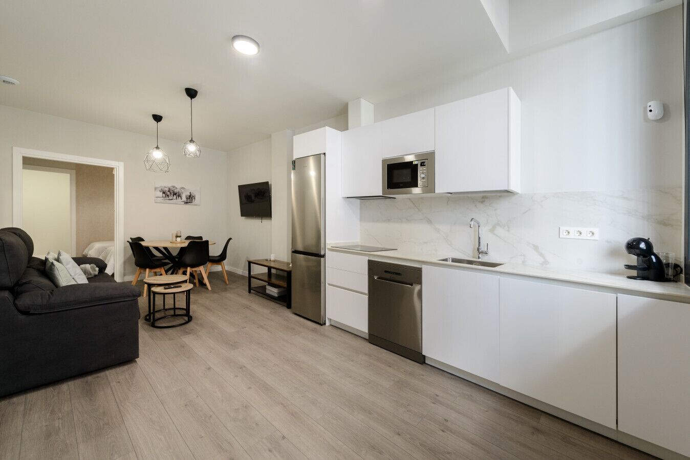 A modern kitchen with white cabinets, stainless steel appliances, and a dining area with a black sofa and wooden table.