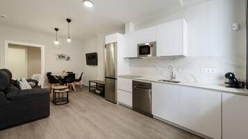 A modern kitchen with white cabinets, stainless steel appliances, and a dining area with a black sofa and wooden table.