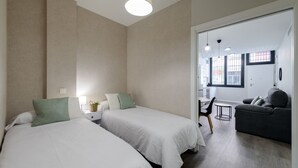 Hotellihuone, jossa on kaksi sänkyä, sohva, pieni pöytä ja näkymä keittiöön ja ruokailutilaan.