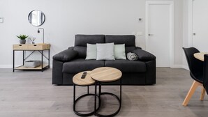 Moderni olohuone, jossa on musta sohva, kaksi pyöreää puista sivupöytää, pieni sivupöytä, jossa on kasvi, ja peili seinällä.
