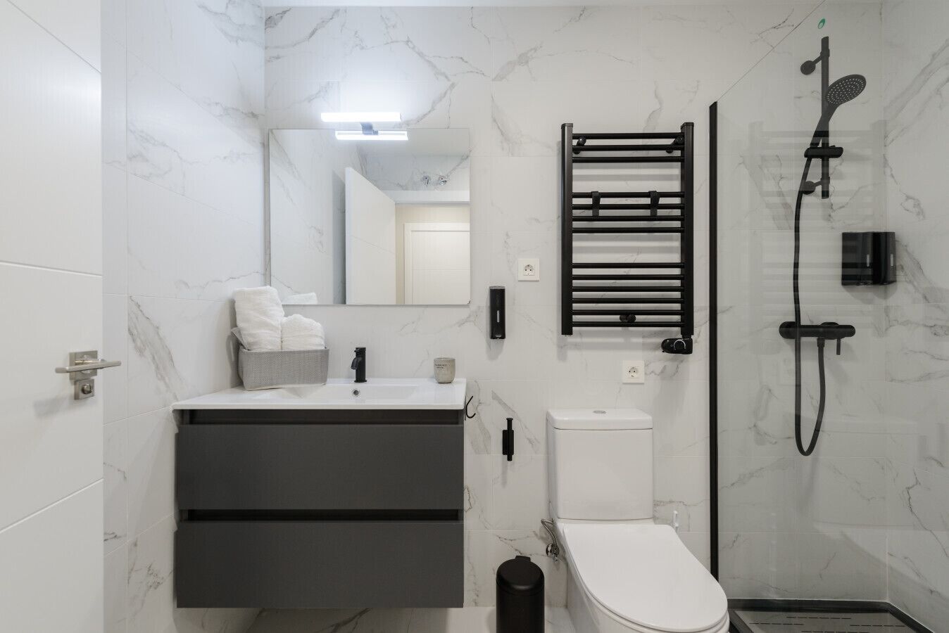 Un baño moderno con pared de mármol, toallero negro, inodoro y ducha.
