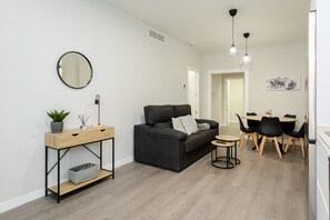 A modern living room with a sofa, a small table, a round mirror, and a dining area with chairs and a table.
