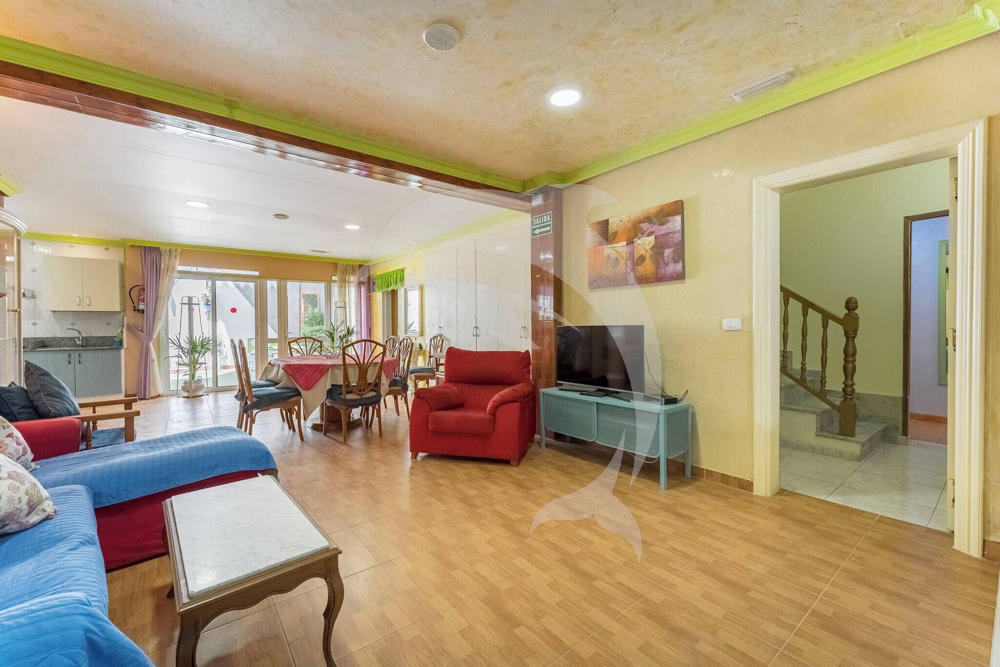 Amplia sala de estar con un conjunto de sofás, un sillón rojo y un televisor sobre un mueble.