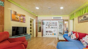 Ein Zimmer mit Fernseher, roten und blauen Sofas, einem Bücherregal und Holzboden.