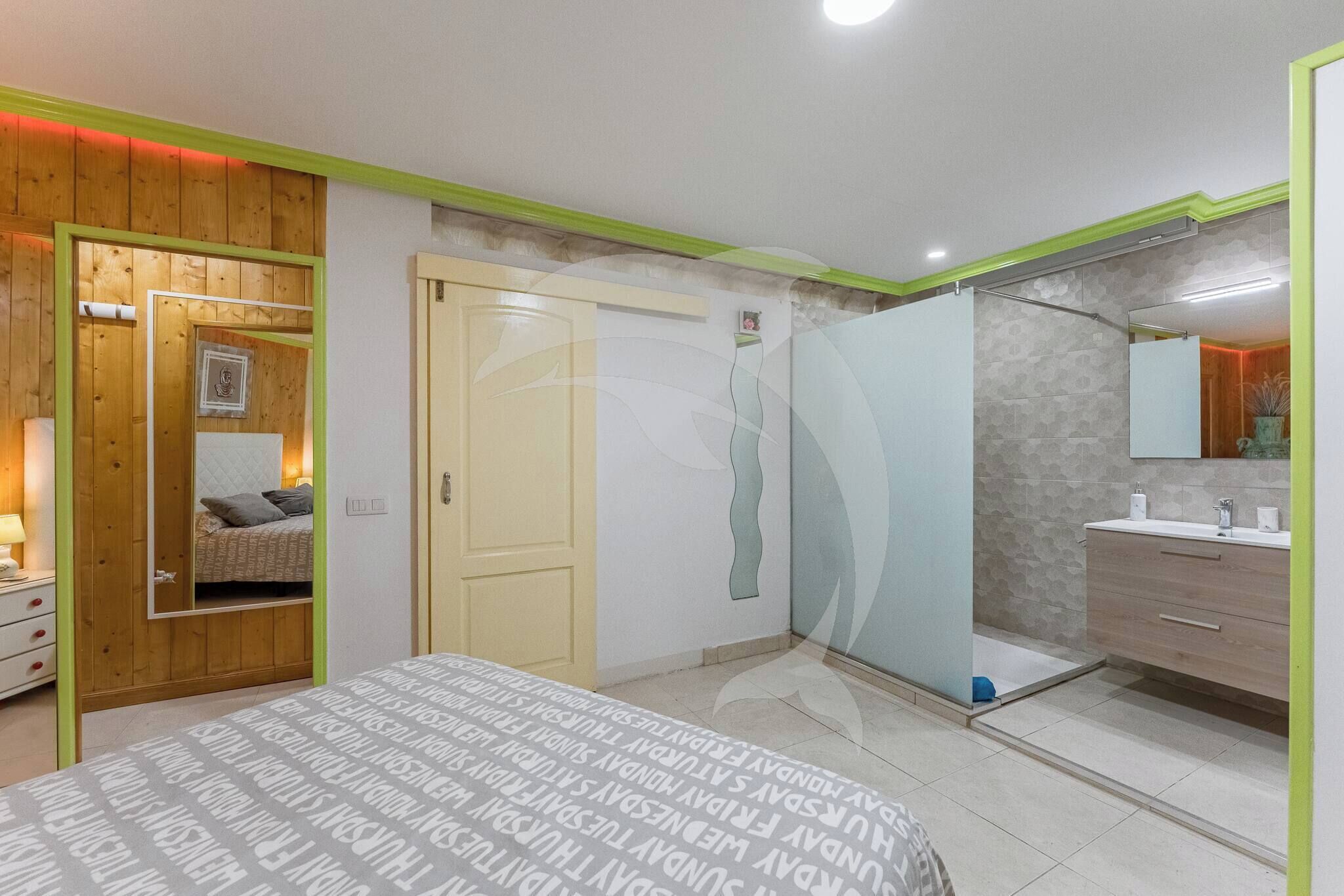 Une chambre moderne comprenant un lit, un miroir, une armoire et une salle de bain avec un lavabo et un miroir.