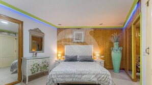 Ein Schlafzimmer mit einem Bett, Nachttischen, einer Kommode, einem großen Spiegel und einem Wandbild.