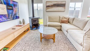 A modern living room with a TV, sofa, coffee table, and a wood-burning stove.