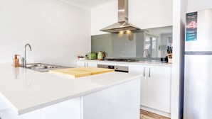A modern kitchen with white cabinetry, a stainless steel range hood, a built-in oven, and a refrigerator.