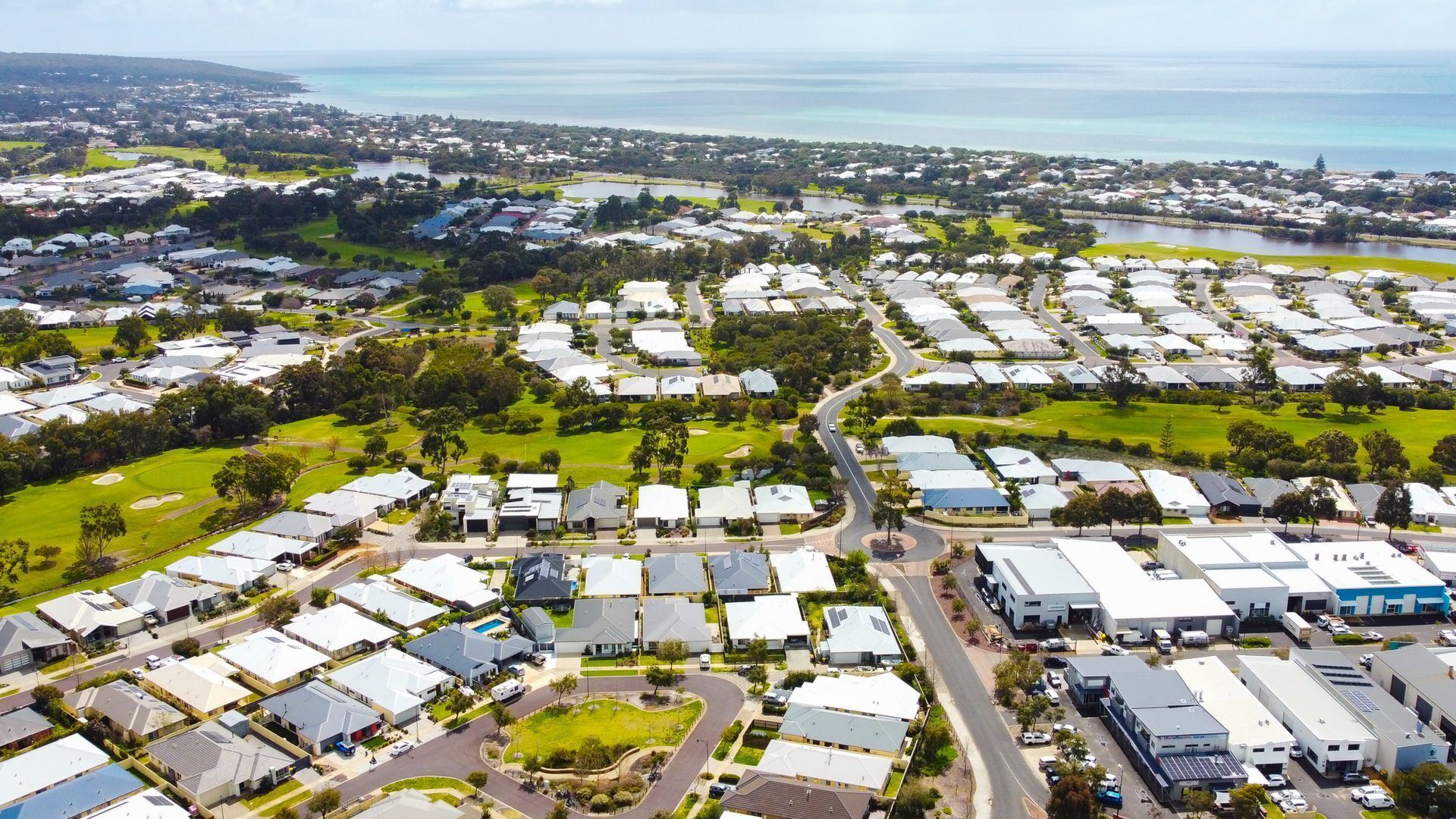 An aerial view of a residential area with multiple detached houses, roads, and a large body of water in the background.